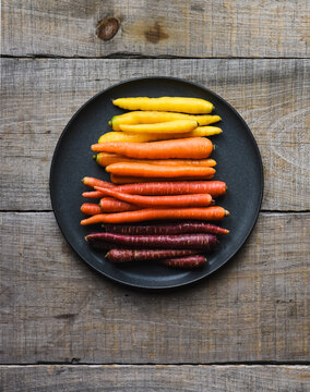 Plate of multicoloured carrots on a wooden background.