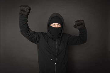 Man in the black hoody with hood wearing balaclava mask with fist up on dark