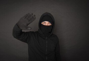 Unrecognizable man in the black hoody with hood wearing balaclava mask holding hand up
