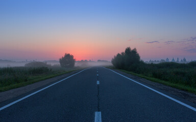 Night Misty Country Road Against Red Dawn on Blue Sky - 565058333