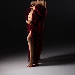 A pregnant woman in a red long dress holds her belly. Maternity dress. Pregnancy. Studio pregnancy photo shoot.