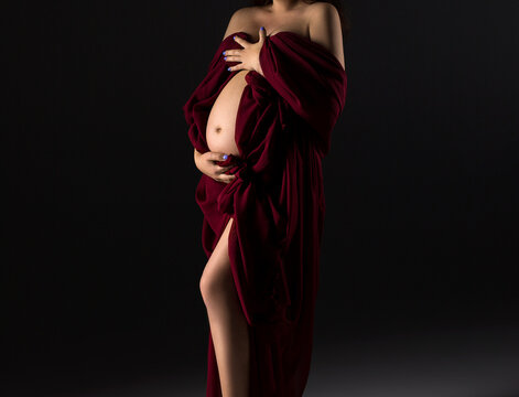 A pregnant woman in a red dress on a grey background. A pregnant belly. Maternity dress. Pregnancy.