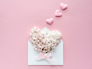 Ein Briefkuvert gefüllt mit weißen Blüten und Herzen auf einem rosa Hintergrund. Grußkarte.