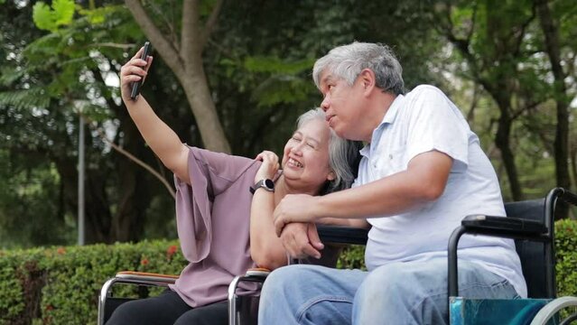 Elderly men and women sitting in wheelchairs in the park. holding smartphones taking pictures together Talk to each other, smile, be happy. Elderly couple. Health care in retirement. senior society