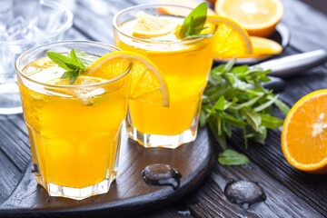 orange cocktail with ice and fresh mint on a black wooden table