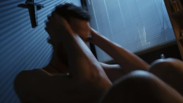 Handheld time-lapse dutch angle shot of young Black military man with PTSD sitting in bedroom having panic attack
