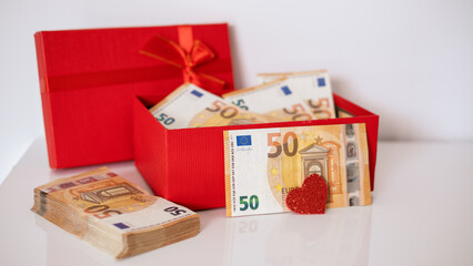 A red gift box filled with Euro currency money.