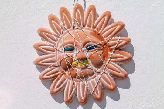 A piece of decoration made in terracotta pottery representing the sun or a flower with a smiley face. It was broken and its pieces are put back together with a white string