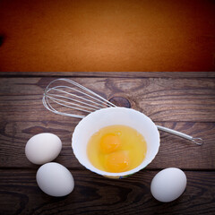 Raw eggs in bowl for whipping on wooden. Baking ingredients.