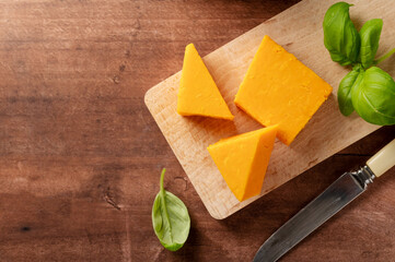 Cheddar orange cheese slices, wooden background, copy space.