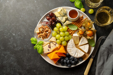 Cheese plate with various cheeses, fruits, nuts and snacks. Dark background, copy space