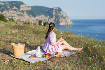 People from behind of a woman in a lilac dress on a picnic enjoying a glass of white wine against the backdrop of mountains and the sea summer mood. Concept: weekend relax vacation summer tourist 