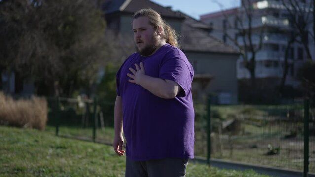 Person having heart attack outdoors. An overweight young man suffering from chest pain unable to breath having to sit down
