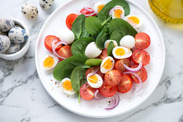 Salad with fresh spinach, cherry tomatoes and boiled quail eggs, horizontal shot on a white marble background, elevated view