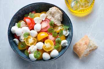 Bowl of tomato salad with mini mozzarella balls, horizontal shot on a light-grey granite background, selective focus