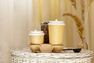 Coffee to go. Coffee composition with two disposable eco friendly cardboard cups on wicker basket in light interior with dry flowers. Takeaway coffee concept. Morning coffee still life. Front view