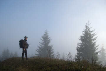 Small figure of lonely hiker enjoying his time on wild forest trail on foggy autumn day