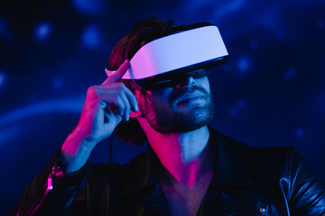 Handsome man in virtual reality glasses, in cyberpunk style in the dark. A guy in a leather jacket in the scenery of the future in neon color flies through space. sitting on a space bike