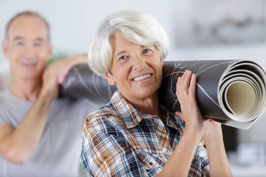 Mature Couple Carrying Carpet In New Room