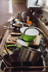 A counter and sink is filled to the brim with dirty dishes. The kitchen is cluttered with bowls,...