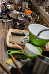 A counter and sink is filled to the brim with dirty dishes. The kitchen is cluttered with bowls, pans, and utensils that need washing. A pile of mess.