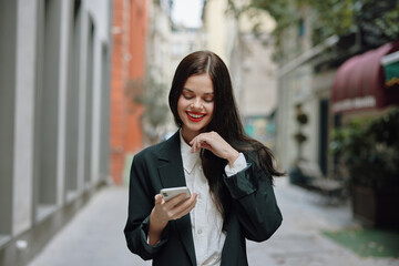 Business brunette woman with red lips smile with teeth with a phone in her hands, white shirt and black jacket fashion on the street, summer trip, vacation in the city tourist freelancer