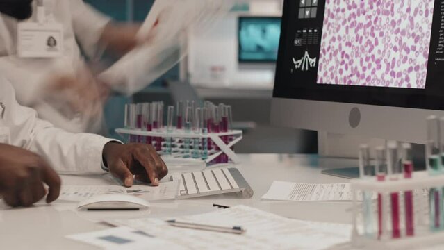Timelapse of close-up of young African American researcher typing on desktop computer keyboard and working with scientific documents with information necessary for clinical experiment