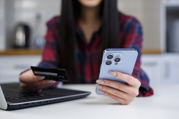 Girl pays with credit card and smartphone app. Young female shopping online with modern mobile phone and bank card