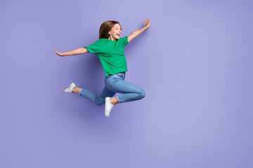 Fototapeta na wymiar Full length photo of impressed sweet small lady wear green t-shirt jumping high arms sides empty space isolated violet color background