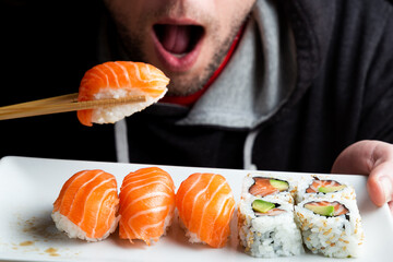 Close up of a young man eating a salmon nigiri with chopsticks