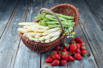 Reife rote Erdbeeren und Spargel aus biologischem Anbau angeboten als close-up in einem Korb auf einem rustikalen alten Holz Board