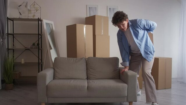 Hard moving. Weak man. Health problem. Casual guy suffering from pain tweaking back when throwing heavy couch himself in light room interior.