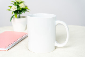 A white blank coffee mug on the top of a white table decorated with minimalistic looks