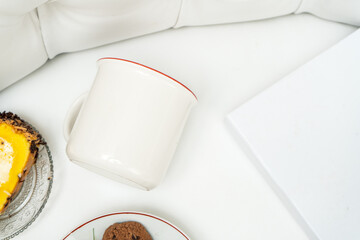 A white blank enamel mug laying out on the top of a white sofa with some snacks placed near it