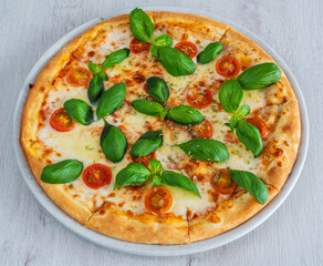 Caprese pizza with suluguni cheese and tomatoes, covered with pesto sauce. On a wooden background in a plate.