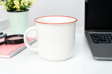 A white blank enamel mug on the top of a white table decorated with tech style
