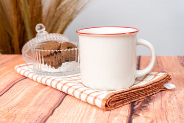 A white blank enamel mug on the top of a hand cloth with some crackers arranged beside it