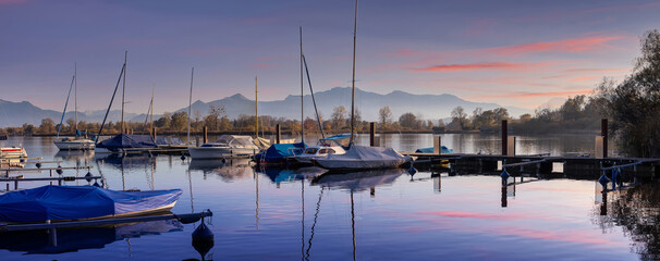 Scenic nature landscape. Sunrise on Chiemsee with vivid sky. Sailboats in the harbor on a summer evening in the sunset. Beautiful alpine summer view near Rimsting at famous Chiemsee, Bavaria, Germany