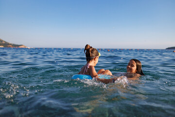 Two sisters in bathing suits play with an inflatable ring in the sea