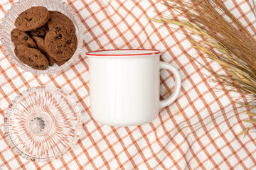 A white blank enamel mug on the top of a hand cloth decorated with simple stuff around it
