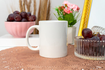 A white blank coffee mug on the top of a rounded mat decorated with simple stuff around it