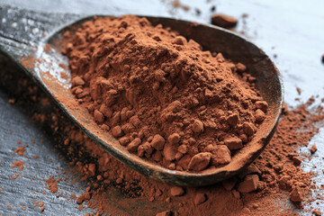 Cocoa powder on a wooden spoon on black background, close-up