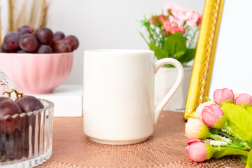 A white blank coffee mug on the top of a rounded mat decorated with simple stuff around it