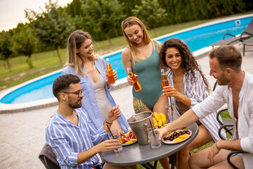 Group of young people cheering with cider by the pool in the garden