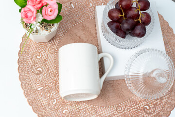 A white blank coffee mug on the top of a rounded mat decorated with simple stuff around it
