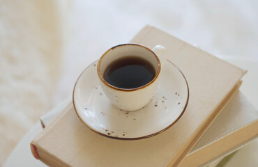 A mug of black coffee stands on a stack of books on the table