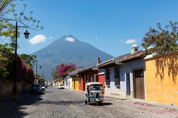 Street with TucTuc in Antigua Guatemala and Volcano Agua - 565091397