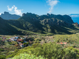 Fototapeta na wymiar Dramatic lush green picturesque valley with old village Los Carrizales . Landscape with sharp rock formation, hills and cliffs seen from mountain road, Tenerife, Canary Islands, Spain. sunny winter