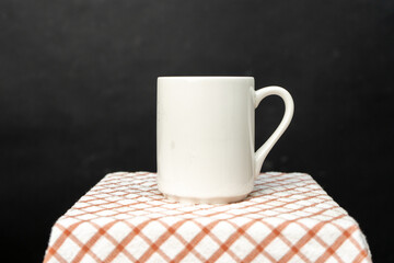 A white blank coffee mug on the top of a hand cloth isolated with black color as the background