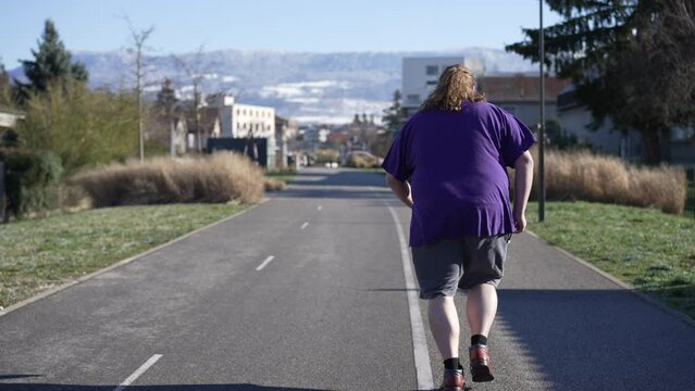 Back of One young overweight man jogging outdoors. Tracking shot of a chubby male person running. Getting back to shape concept